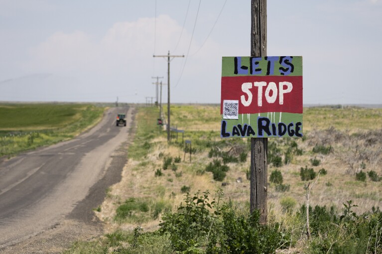 A tractor travels down Hunt Road in front of a "Let's Stop Lava Ridge" sign near the Minidoka National Historic Site, Thursday, July 6, 2023, in Jerome, Idaho. (AP Photo/Lindsey Wasson)