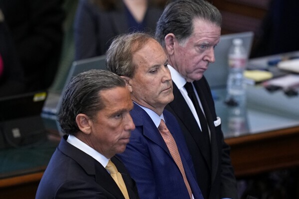 Texas state Attorney General Ken Paxton, center, stands between his attorneys Tony Buzbee, front, and Dan Cogdell, rear, as the articles of his impeachment are read during the his impeachment trial in the Senate Chamber at the Texas Capitol, Tuesday, Sept. 5, 2023, in Austin, Texas. (AP Photo/Eric Gay)
