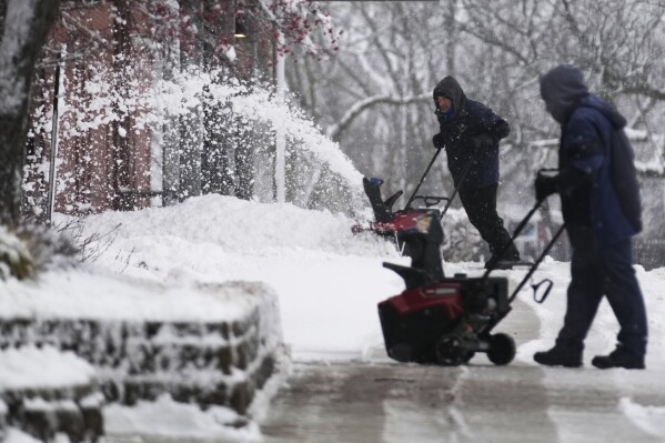 People clean a path from snow in front of a school in Wheeling, Ill., Friday, Jan. 12, 2024. (AP Photo/Nam Y. Huh)