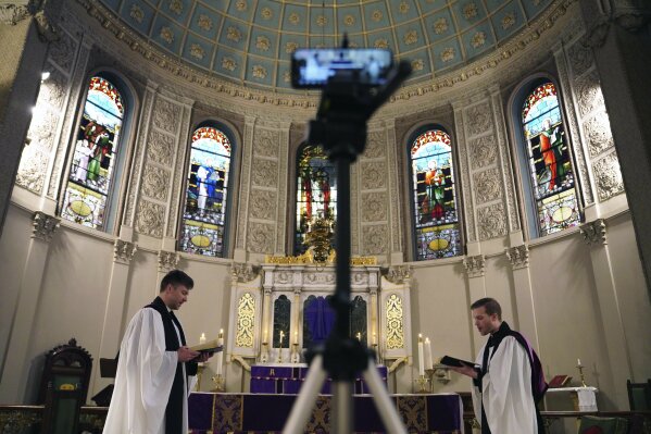 In this March 29, 2020 photo, the Rev. Steven Paulikas, right, and curate Spencer Cantrell deliver an Evening Prayer service over Facebook Live in the Brooklyn borough of New York. The global COVID-19 coronavirus pandemic is upending the season's major religious holidays, forcing leaders and practitioners across faiths to improvise. (AP Photo/Emily Leshner)