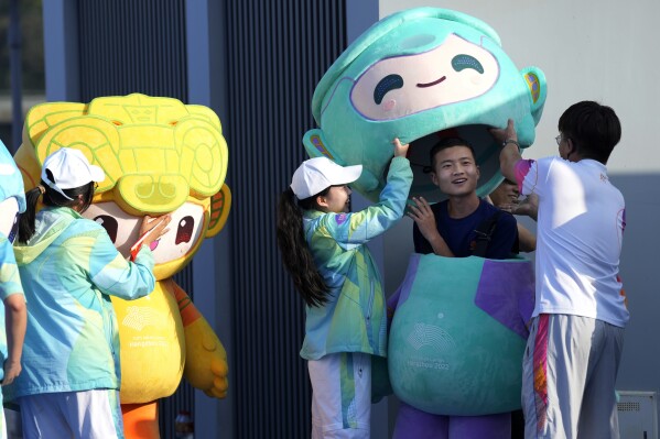 A worker with a costume of Lianlian, one of three Hangzhou Asian Games mascots, is help to prepare for the award ceremony of men's beach volleyball at the 19th Asian Games in Ningbo, China, Thursday, Sept. 28, 2023. (AP Photo/Eugene Hoshiko)