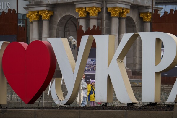 A woman and child walk behind a "I Love Ukraine" sign in Kyiv, Ukraine, Thursday, March 14, 2024. Ukraine fired at least eight missiles at Russia's Belgorod border region, killing one person and wounding six, local officials said Thursday, as Kyiv's forces apparently kept up their efforts to rattle the Kremlin on the eve of Russia's presidential election, a vote that is taking place amid a ruthless crackdown on dissent. (AP Photo/Vadim Ghirda)