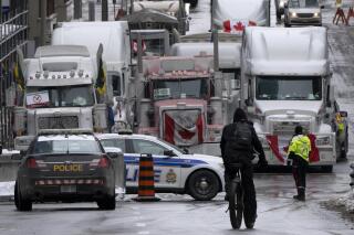 A cyclist rides towards a police barricade where trucks are lined up near Parliament hill on Wednesday, Feb. 2, 2022 in Ottawa. On Monday, Feb. 7, 2022, The Associated Press reported on posts circulating online that falsely claimed 50% of Ottawa police officers had resigned in response to protests against vaccine mandates. (Adrian Wyld /The Canadian Press via AP)