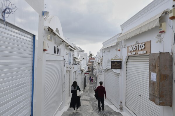 Tourists pass by closed shops in Fira town as Greek authorities are taking emergency measures in response to intense seismic activity on the popular Aegean Sea holiday island of Santorini, southern Greece, Monday, Feb. 3, 2025. (AP Photo/Petros Giannakouris)