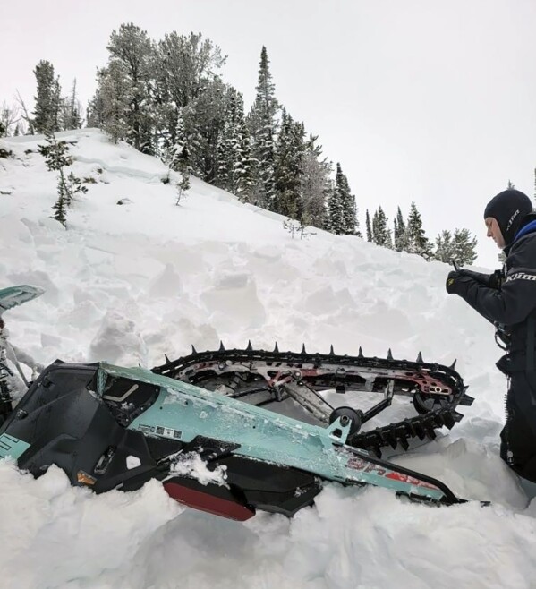 Mark Fossum is seen taking a picture of a snowmobile that was flipped over in an avalanche in the Montana backcountry, Jan 29, 2024, near Cooke City, Mont. The rider of the snowmobile deployed an inflatable airbag and survived. (Wesley Mlaskoch via AP)
