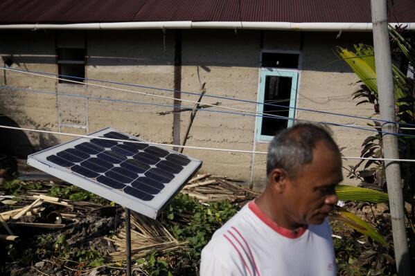 A man walks past a small solar panel he uses for back up, outside his house on Karampuang Island, in West Sulawesi, Indonesia, Thursday, Dec. 22, 2022. While Indonesia has vast renewable and green energy potential from solar, wind, geothermal and other sources, experts warn that the vast archipelago nation faces unique financial, policy, infrastructure and other challenges that will require innovation.(AP Photo/Dita Alangkara)