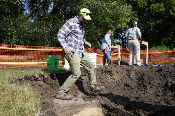 Nebraska State Archeologist Dave Williams walks in a hole as workers dig for the suspected remains of children who once attended the Genoa Indian Industrial School, Tuesday, July 11, 2023, in Genoa, Neb. The mystery of where the bodies of more than 80 children are buried could be solved this week as archeologists dig in a Nebraska field that a century ago was part of a sprawling Native American boarding school. (AP Photo/Charlie Neibergall)