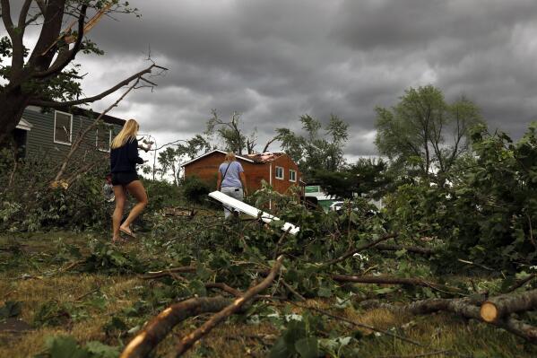 Residents walk past damaged houses and fallen trees after a tornado passed through the area on Monday, June 21, 2021 in Woodridge, Ill. (AP Photo/Shafkat Anowar)