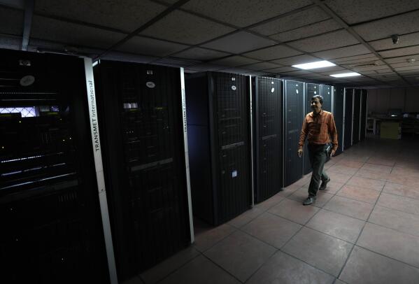 An employee at the India Meteorological Department walks past a line of servers in a communication room for national and international data in New Delhi, India, Friday, March 17, 2023. The India Meteorological Department as well as the state of Kerala have increased infrastructure for cyclone warnings since Cyclone Ockhi in 2017, which killed about 245 fishermen out at sea. (AP Photo/Manish Swarup)