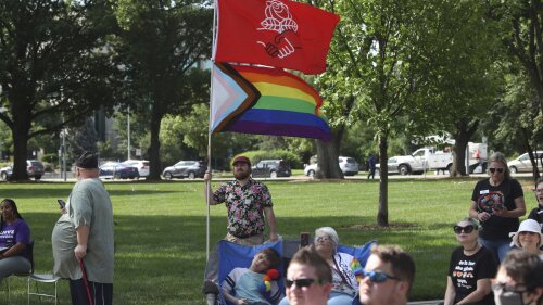 Kirby Evers, a 31-year-old bisexual Lawrence, Kan., resident, displays the red flag of the Democratic Socialists of America and a Pride flag during a rally outside the Kansas Statehouse in favor of transgender rights, Friday, June 30, 2023, in Topeka, Kan. Evers said he believes a U.S. Supreme Court decision allowing a Christian graphic artist to refuse to work with same-sex couples will increase discrimination against LGBTQ people. (AP Photo/John Hanna)