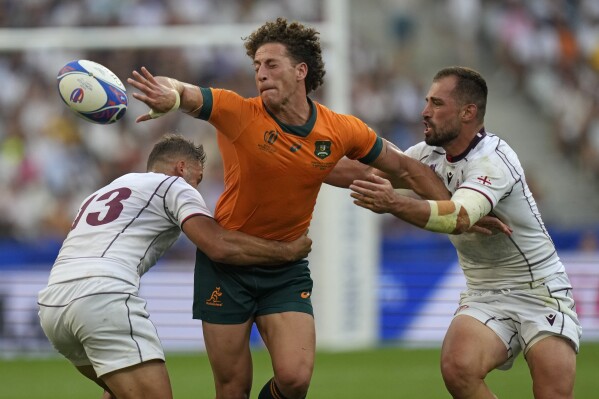 Australia's Mark Nawaqanitawase, center, passes the ball away as he is held up by Georgia's Demur Tapladze, left, during the Rugby World Cup Pool C match between Australia and Georgia at the Stade de France in Saint-Denis, north of Paris, Saturday, Sept. 9 31, 2023. (AP Photo/Thibault Camus)