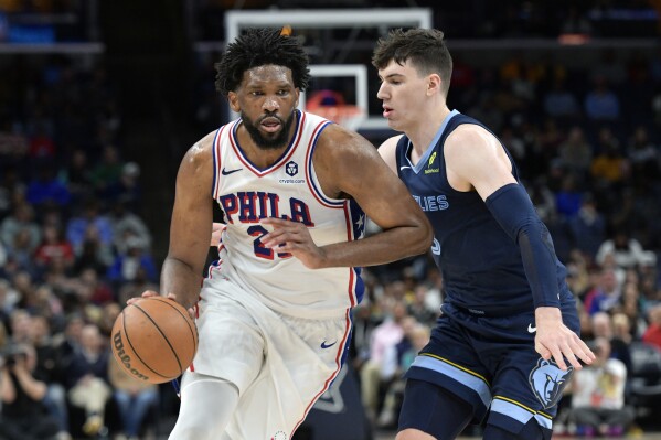 Philadelphia 76ers center Joel Embiid (21) handles the ball against Memphis Grizzlies forward Jake LaRavia in the second half of an NBA basketball game Wednesday, Nov. 20, 2024, in Memphis, Tenn. (AP Photo/Brandon Dill)