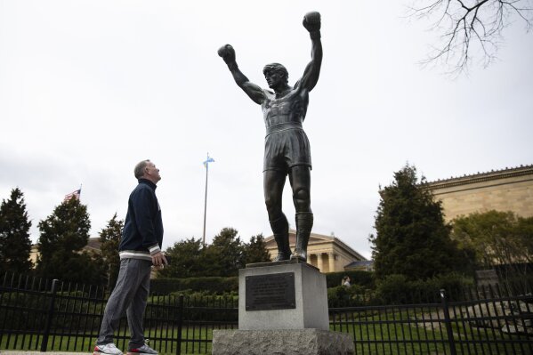 In this April 3, 2020, photo, Timothy Frank visits the Rocky Statue at the Philadelphia Art Museum in Philadelphia. “Rocky” finished tied for No. 2 in The Associated Press Top 25 favorite sports movies poll. (AP Photo/Matt Rourke)