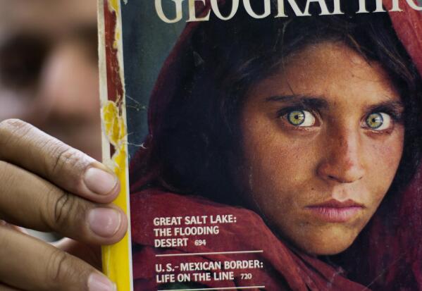 FILE - In this file photo taken on Oct. 26, 2016, Pakistan's Inam Khan, owner of a book shop shows a copy of a magazine with the photograph of Afghan refugee woman Sharbat Gulla, from his rare collection in Islamabad, Pakistan. National Geographic’s famed green-eyed “Afghan Girl” has arrived in Italy as part of the West’s evacuation of Afghans following the Taliban takeover of the country, the Italian government said Thursday. The office of Premier Mario Draghi said Italy had organized the evacuation of Sharbat Gulla after she asked to be helped to leave the country. The Italian government will now help to welcome her and get her integrated into life here, the statement said.(AP Photo/B.K. Bangash, File)