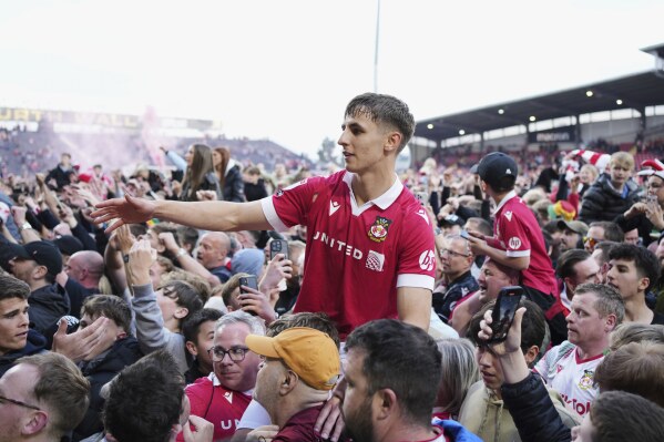 Wrexham's Max Cleworth celebrates with teammates and fans as they win the English League One soccer match between Wrexham and Charlton Athletic at the Racecourse ground in Wrexham, Wales, Saturday, April 26, 2025. (AP Photo/Jon Super)