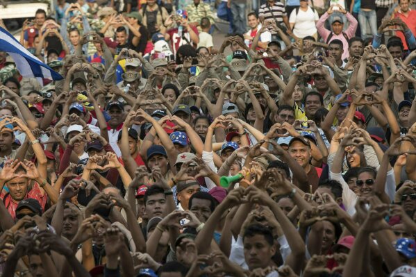 
              Government supporters flash heart-hand signals during the "Hands off Venezuela" concert at the Tienditas International Bridge, in Venezuela on the border with Colombia, Friday, Feb. 22, 2019.  Venezuela's power struggle is set to convert into a battle of the bands Friday when musicians demanding Nicolas Maduro allow in humanitarian aid and those supporting the embattled leader's refusal sing in rival concerts being held at both sides of a border bridge where tons of donated food and medicine are being stored. (AP Photo/Rodrigo Abd)
            