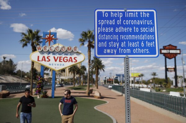 FILE - In this March 21, 2020 file photo, a sign advises people to practice social distancing to slow the spread of the coronavirus at the "Welcome to Fabulous Las Vegas Nevada" sign amid a shutdown of casinos along the Las Vegas Strip in Las Vegas. Nervous travelers, spotty air service, health risks _  the battered global tourism industry is facing unprecedented uncertainty in the wake of the new coronavirus. Millions of workers are laid off or furloughed, and it will likely take years for the industry to get back to the strong demand it was seeing just six months ago. (AP Photo/John Locher, File)
