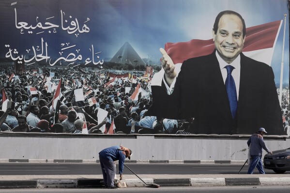 Workers clean the street under a billboard supporting Egyptian President Abdel Fattah el-Sissi for the presidential elections, in Cairo, Egypt, Sunday, Dec. 10, 2023. Egyptians began voting Sunday in a presidential election in which President Abdel Fattah el-Sissi, who faces no serious challenger, is certain to win another term, keeping him in power until 2030. Arabic reads,