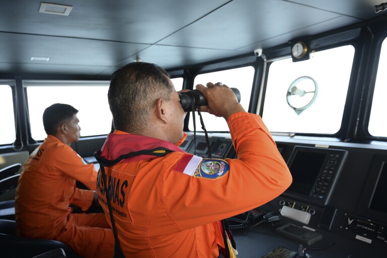 A member of the National Search and Rescue Agency uses binoculars to scan the horizon during the search for a boat carrying Rohingya refugees reportedly capsized in the waters off West Aceh, Indonesia, Thursday, March 21, 2024. A wooden boat carrying dozens of Rohingya Muslims capsized off Indonesia's northernmost coast on Wednesday, according to local fishermen who rescued six people. (AP Photo/Reza Saifullah)
