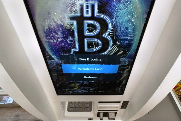 FILE - The Bitcoin logo appears on the display screen of a cryptocurrency ATM in Salem, N.H., Feb. 9, 2021. The U.S. for the first time has given the greenlight to almost a dozen exchange traded funds for bitcoins. ETFs give every day investors a way to get in on trading in oil, gold, corporate bonds and now bitcoin without actually having to own a bar of gold, a barrel of oil, or a bitcoin. (AP Photo/Charles Krupa, File)