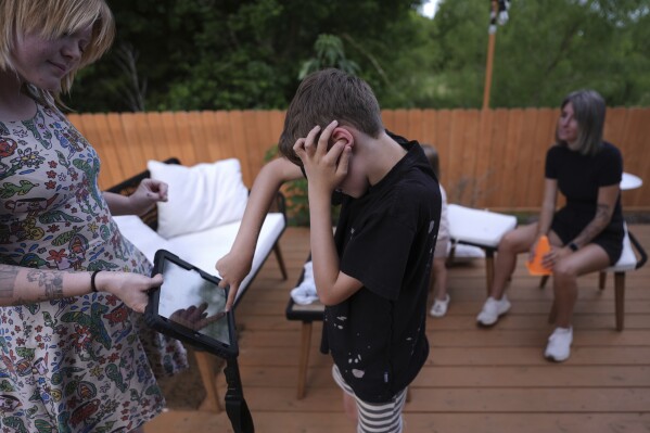 Charlie Lamb, who is diagnosed with autism and is non-verbal, uses an AAC device to communicate with a caregiver, Monday, May 12, 2025, in Austin, Texas. (AP Photo/Eric Gay)