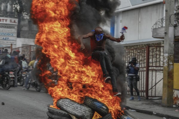 A protester jumps burning tires during a protest against Haitian Prime Minister Ariel Henry in Port-au-Prince, Haiti, Monday, Feb. 5, 2024. (AP Photo/Odelyn Joseph)