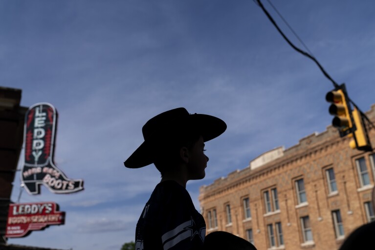 A boy wears a cowboy hat while sitting on his father's shoulders as they walk through the Stockyards National Historic District which holds twice daily cattle drives for visitors in Forth Worth, Texas, Friday, April 21, 2023. As early as the 1600s, ranchers were raising thousands of cattle in the region, and as they expanded their herds and drew more settlers to the area, they built the foundation of what would become an independent country and then the 28th U.S. state. (AP Photo/David Goldman)