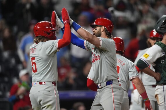 Philadelphia Phillies' Bryson Stott, left, congratulates Bryce Harper for a three-run home run off Colorado Rockies relief pitcher John Curtiss during the eighth ninth inning of a baseball game Saturday, May 25, 2024, in Denver. (AP Photo/David Zalubowski)