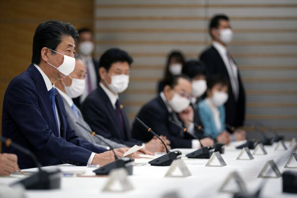 Japanese Prime Minister Shinzo Abe, left, speaks during a meeting of the headquarters for measures against the coronavirus disease at the prime minister official residence in Tokyo, Japan, Monday, April 6, 2020. Abe said that he will declare a state of emergency for Tokyo and six other prefectures as early as Tuesday to bolster measures to fight the coronavirus outbreak, but that there will be no hard lockdowns. (Franck Robichon/Pool Photo via AP)