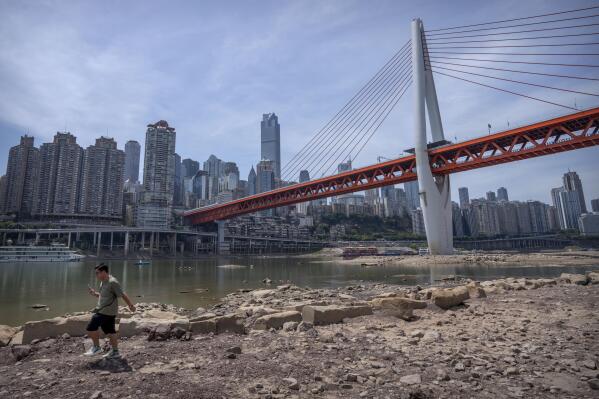 A man walks along the lower than normal bank of the Jialing River in southwestern China's Chongqing Municipality, Friday, Aug. 19, 2022. Ships crept down the middle of the Yangtze on Friday after the driest summer in six decades left one of the mightiest rivers shrunk to barely half its normal width and set off a scramble to contain damage to a weak economy in a politically sensitive year. (AP Photo/Mark Schiefelbein)