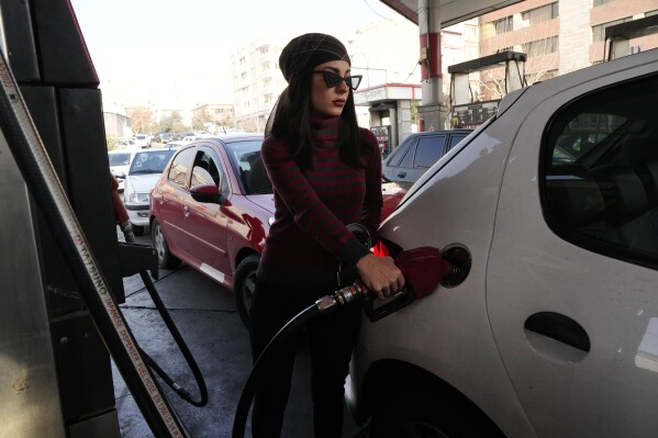 A woman fills her car at a gas station in Tehran, Iran, Monday, Dec. 18, 2023. Nearly 70% of Iran's gas stations went out of service on Monday following possible sabotage — a reference to cyberattacks, Iranian state TV reported. (AP Photo/Vahid Salemi)