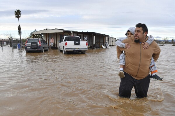 FILE - Ryan Orosco, of Brentwood, carries his son Johnny, 7, on his back while his wife Amanda Orosco waits at the front porch to be rescued from their flooded home on Bixler Road in Brentwood, Calif., Jan. 16, 2023. The National Oceanic and Atmospheric Administration announced Monday, Sept. 11, that there have been 23 weather extreme events in America that cost at least $1 billion this year through August, eclipsing the year-long record total of 22 set in 2020. (Jose Carlos Fajardo/Bay Area News Group via AP, File)