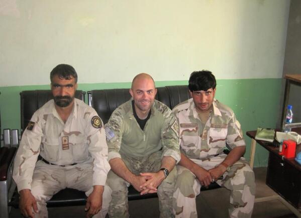In this undated photo provided by Ryan Brummond, U.S. Special Forces Officer Ryan Brummond, center, is seated next to Mohammad Khalid Wardak, right, in Afghanistan. Khalid, as he's called by his friends, had no intention of leaving Afghanistan, where he was a high-profile national police officer who'd worked alongside American special forces to defeat the Taliban. Then with stunning speed, his government collapsed. Now he is in hiding with his wife and four children, wounded and hunted by the Taliban, desperately hoping that American officials will repay his loyalty by helping his family escape almost certain death. (Ryan Brummond via AP)