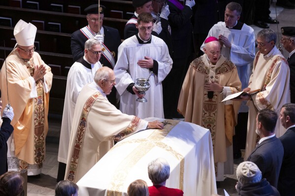 Deacon Paul Cerio places a cross on the casket of Rev. Stephen Gutgsell during his funeral at St. Cecilia Cathedral in Omaha, Neb., on Monday, Dec. 18, 2023. Gutgsell was killed in the rectory of St. John the Baptist Church in Fort Calhoun on Dec. 10. (Chris Machian/Omaha World-Herald via AP)