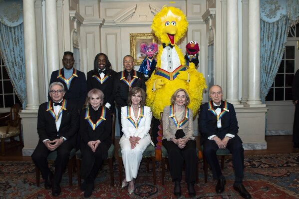 Front row from left, 2019 Kennedy Center Honorees Michael Tilson Thomas, Linda Ronstadt, Sally Field, Joan Ganz Cooney, and Lloyd Morrisett, back row from left, Philip Bailey, Verdine White, Ralph Johnson, and characters from "Sesame Street," Abby Cadabby, Big Bird, and Elmo pose for a group photo following the Kennedy Center Honors State Department Dinner at the State Department on Saturday, Dec. 7, 2019, in Washington. (AP Photo/Kevin Wolf)
