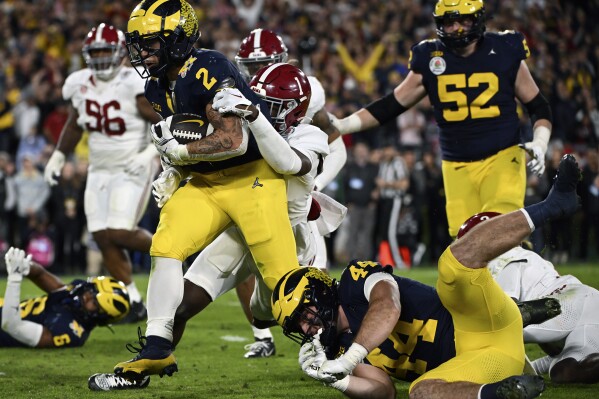 FILE - Michigan running back Blake Corum (2) runs in for a touchdown past Alabama defensive back Kool-Aid McKinstry (1) during overtime at the Rose Bowl CFP NCAA semifinal college football game Jan. 1, 2024, in Pasadena, Calif. Nonprofits Hail! Impact, which supports the University of Michigan's Wolverines, and Montlake Futures, which supports athletes at the University of Washington, are set to benefit regardless of who wins the national championship. (AP Photo/Kyusung Gong, File)