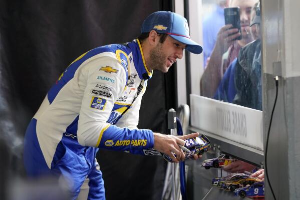 Chase Elliott, left, signs autographs and interacts with fans in the Fan Zone from his garage during practice for the Daytona 500 auto race at Daytona International Speedway, Saturday, Feb. 19, 2022, in Daytona Beach, Fla. (AP Photo/John Raoux)