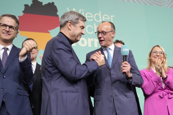 Friedrich Merz, with the microphone, the candidate of the mainstream conservative Christian Democratic Union party, shakes hands with Markus Soeder, leader of CSU and Minister-President of Bavaria, at the party headquarters in Berlin, Germany, Sunday, Feb. 23, 2025, after the German national election. (AP Photo/Markus Schreiber)