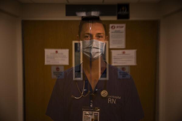 In this photo created with an in-camera multiple exposure, registered nurse Anthony Wilkinson, part of a group of nurses who had been treating coronavirus patients in an intensive care unit, stands for a photo in the empty COVID-19 ICU at Providence Mission Hospital in Mission Viejo, Calif., Tuesday, April 6, 2021. Wilkinson still thinks about those 30 hours — the ones when three patients died. "You try to keep somebody alive, but their body is decomposing," says Wilkinson. (AP Photo/Jae C. Hong)