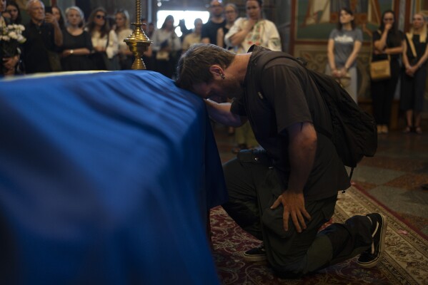 A mourner kneels while paying his final respects for Ukrainian writer Victoria Amelina during a memorial service for Amelina in Kyiv, Ukraine, Tuesday, July 4, 2023. The award-winning writer was killed in June by a Russian missile attack on a popular restaurant frequented by journalists and aid workers in eastern Ukraine. (AP Photo/Jae C. Hong)