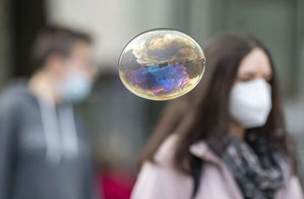 A soap bubble flies in front of people with mouth and nose protection in Stuttgart, Germany, Friday, Oct. 9, 2020. Chancellor Merkel is discussing the situation with the mayors of the eleven largest German cities in view of the sharp rise in corona figures. (Sebastian Gollnow/dpa via AP)