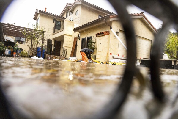 A resident attempts to protect his home as floodwaters rise during a rainstorm, Sunday, Feb. 4, 2024, in Santa Barbara, Calif. (AP Photo/Ethan Swope)