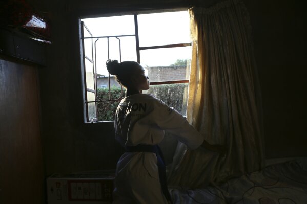 Natsiraishe Maritsa opens the curtains inside her room in the Epworth settlement about 15 km southeast of the capital Harare, Saturday Nov. 7, 2020. In Zimbabwe, where girls as young as 10 are forced to marry due to poverty or traditional and religious practices, a teenage martial arts fan 17-year old Natsiraishe Maritsa is using the sport to give girls in an impoverished community a fighting chance at life. (AP Photo/Tsvangirayi Mukwazhi)