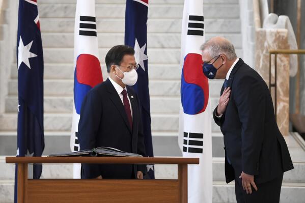 South Korean President Moon Jae-in, left, is invited to sign a visitor's book by Australian Prime Minister Scott Morrison at Parliament House, in Canberra, Australia, Monday, Dec. 13, 2021. Moon is on a two-day official visit to Australia. (Lukas Coch/Pool Photo via AP)