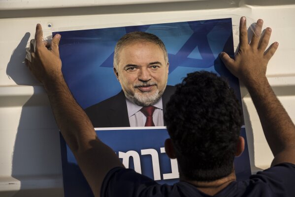 FILE - In this Tuesday, Sept. 17, 2019 file photo, a supporter of the Yisrael Beiteinu right-wing nationalist party, hangs an election poster of its leader, Avigdor Lieberman, outside a polling station, in the West Bank settlement of Nokdim. For the sixth time in his lengthy political career, Benjamin Netanyahu has been tasked by Israel’s president to form a new government. Lieberman who emerged even stronger in last week’s vote with eight seats has stood firm on his demand for a secular unity government between the two major parties, Likud and Benny Gantz’s Blue and White. (AP Photo/Tsafrir Abayov, File)