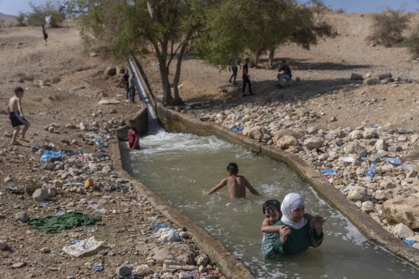 Palestinians cool down in a spring in Auja in the Jordan Valley on Wednesday, Aug.9, 2023. In the occupied West Bank, where Israeli water pipes don’t reach, Palestinians say they can't get enough water to irrigate their farms. By comparison, the neighboring Jewish settlements look like an oasis with swimming pools. (AP Photo/Ohad Zwigenberg)