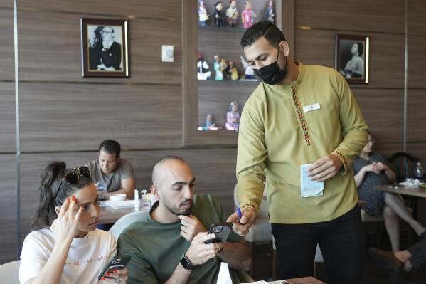 Ali el-Sayyed Mohammed takes an order from customers at Hadoota Masreya Restaurant in Dubai, United Arab Emirates, Sept. 5, 2022. Mohammed left his hometown of Beheira along the Egyptian Nile Delta this year to come to Dubai in the hopes of earning a living wage. The 26-year-old said he is supporting his mother and sisters back home and hoping to save enough to get married. (AP Photo/Malak Harb)