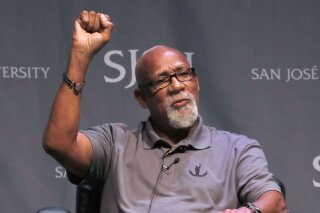 FILE - In this Oct. 17, 2018, file photo, 1968 Olympic athlete John Carlos raises his fist as he speaks about his experience as Olympians who participated in Mexico City in 1968 during the 50th Anniversary of the Defining Moment in Sports Social Activism Historic Town Hall at San Jose State University in San Jose, Calif. Olympic protestor John Carlos co-authored a letter with an influential American athletes' group calling on the IOC to abolish the rule that bans protests at the Olympics and replace it with a policy written in collaboration with athletes. Carlos and Tommie Smith raised their fists on the medals stand at the 1968 Olympics to protest racial inequality in the United States.  (AP Photo/Tony Avelar, File)
