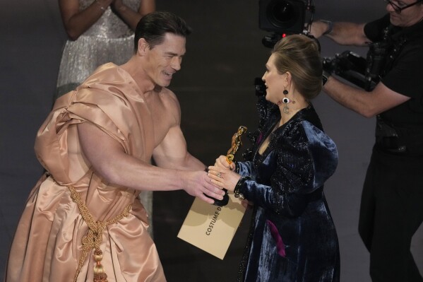 John Cena, left, presents the award for best costume design to Holly Waddington for "Poor Things"during the Oscars on Sunday, March 10, 2024, at the Dolby Theatre in Los Angeles. (AP Photo/Chris Pizzello)