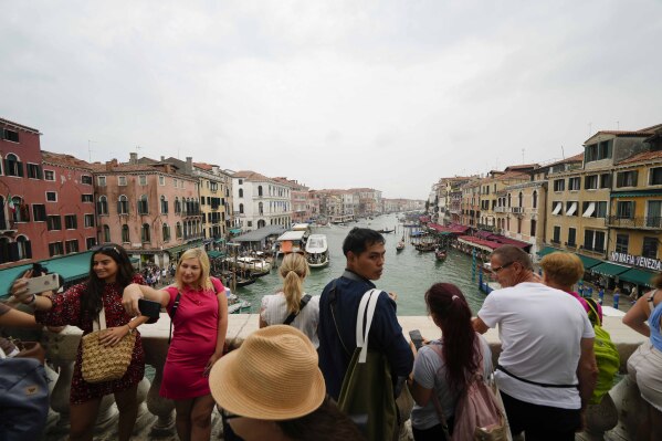 FILE -Tourists visit Rialto bridge, in Venice, Italy, Wednesday, Sept. 13, 2023. Day-trippers to the lagoon city who fail to pay 5 euros ($5.43) to enter the lagoon city’s historic center during a limited-date pilot program launching later this month will face fines starting at 10 times the entrance fee, officials said Thursday, April 4, 2024. (AP Photo/Luca Bruno, File)